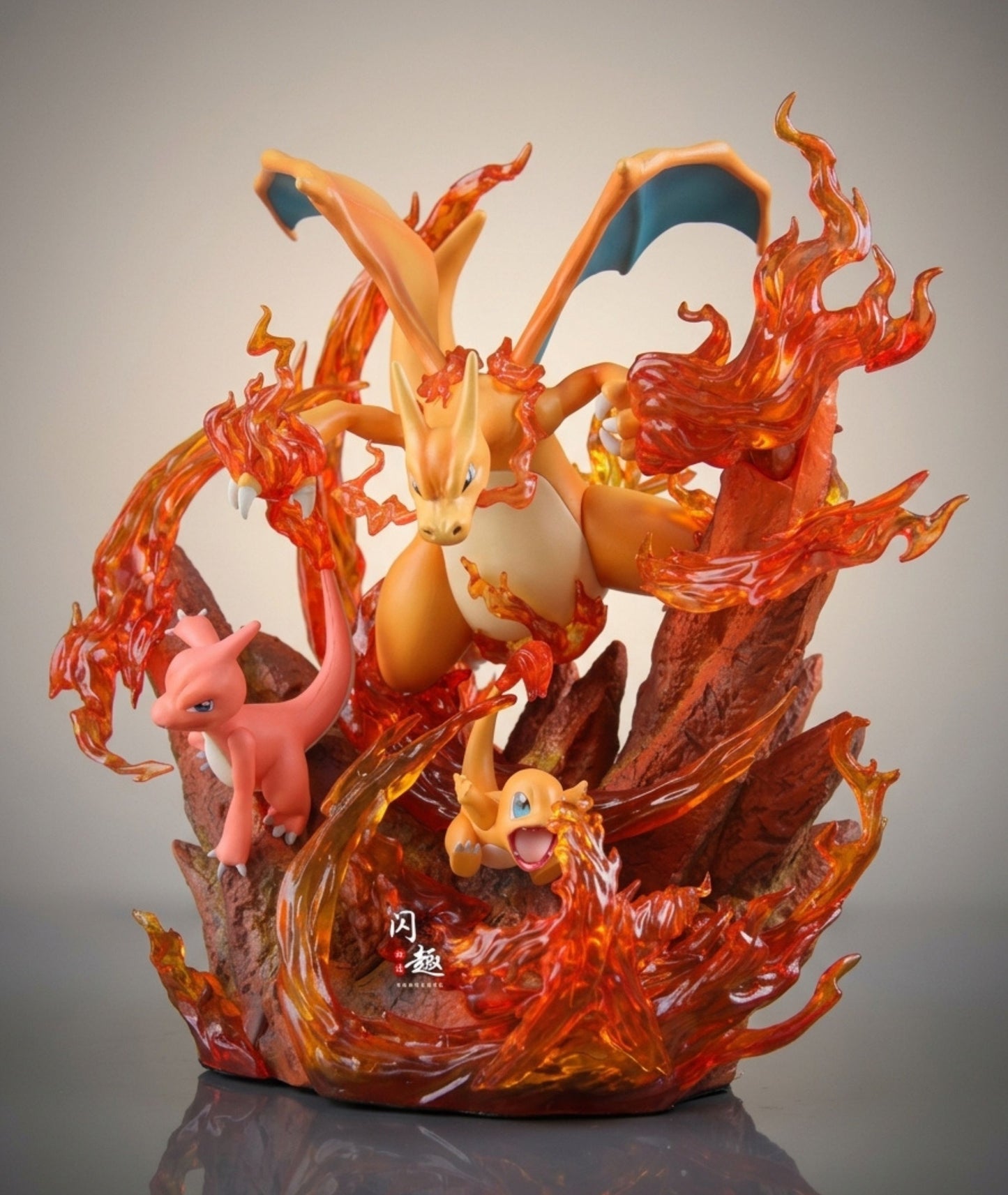 A detailed collectible figurine of Charizard, Mew, and Chikorita emerging from translucent orange flames on a dark base, photographed against a neutral gray studio background.