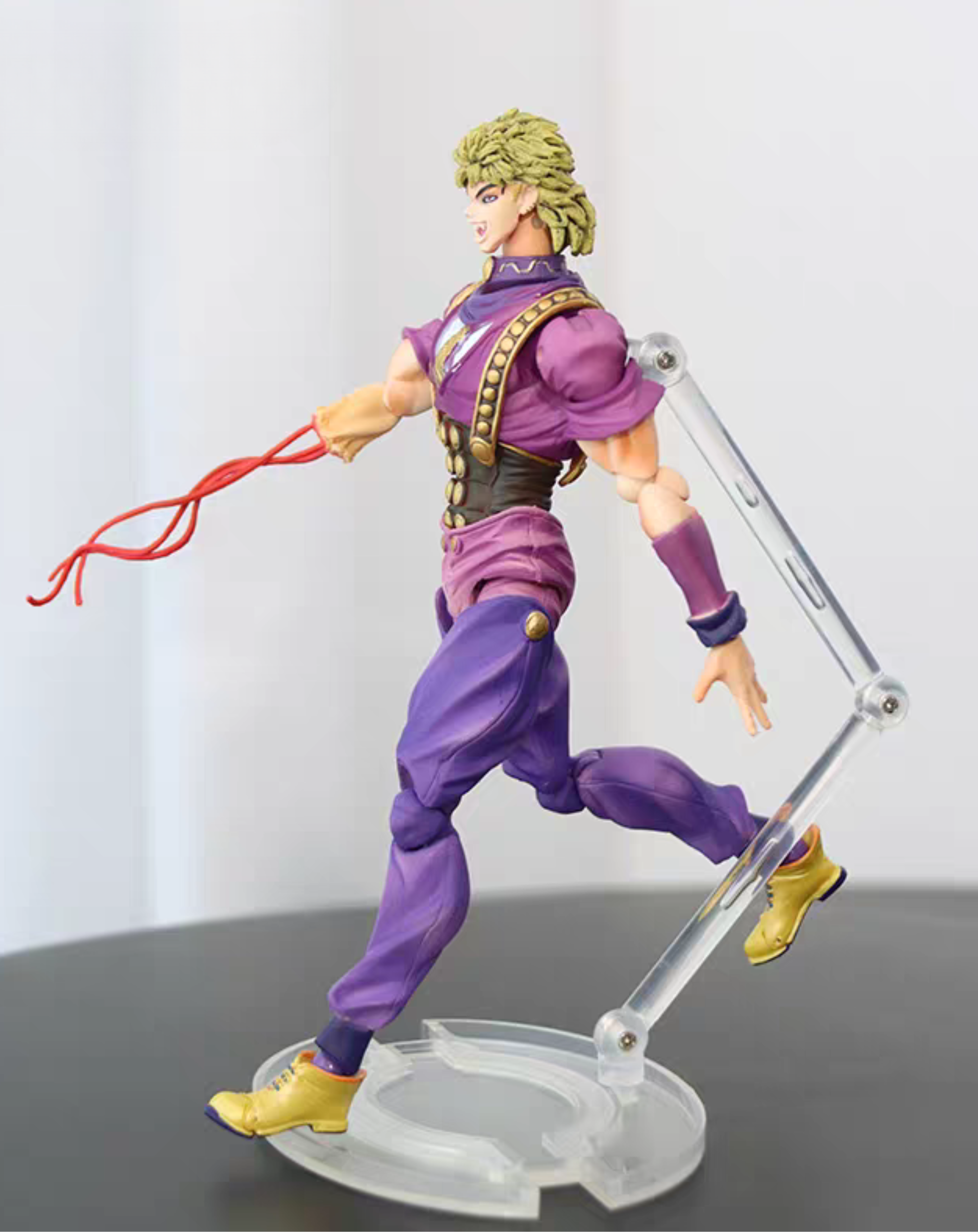 Dio Brando JoJo's Bizarre Adventure figure in a dynamic action pose with red energy effect, three-quarter angle on the clear stand