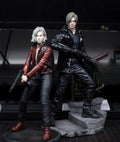 Leon Kennedy Grace Ashcroft Resident Evil action figures posed together on a display base against a dark studio background. The figure on the left has silver hair and wears a red jacket with black pants and boots, holding a gun.