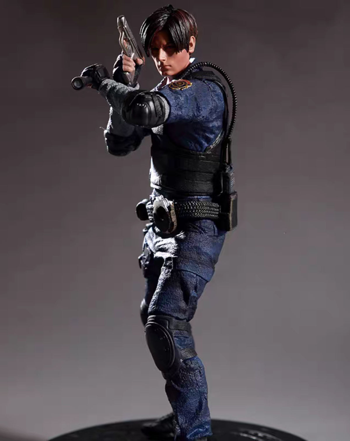 A detailed Leon Kennedy from Resident Evil in a tactical blue uniform with black gear, holding a pistol, posed on a dark studio background.