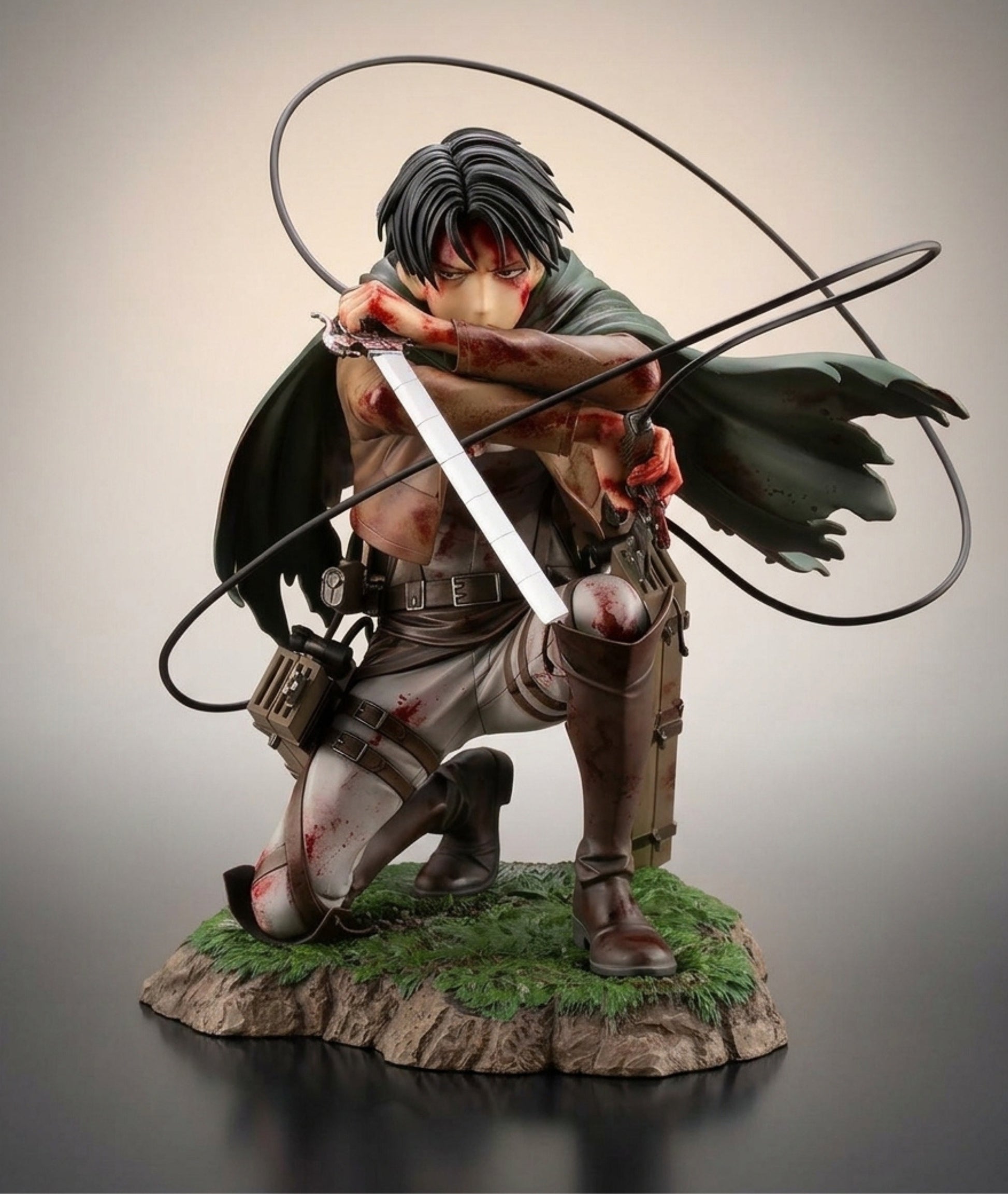Attack on Titan anime collectible statue of Levi Ackerman in a crouching combat pose, holding a sword with a black energy ring in front of him, set on a rocky base with green grass.