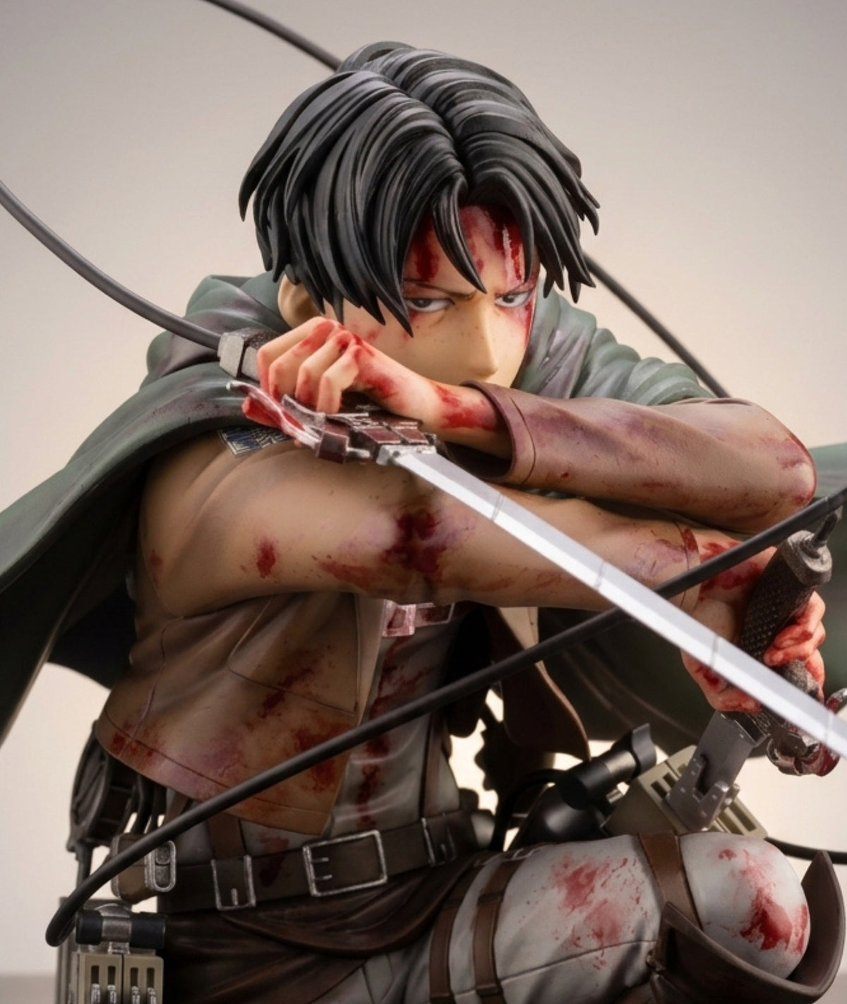 Attack on Titan anime figure of Levi Ackerman in a crouched combat pose, holding a sword, with blood splatters on his face, arms, and clothing against a plain light gray background.