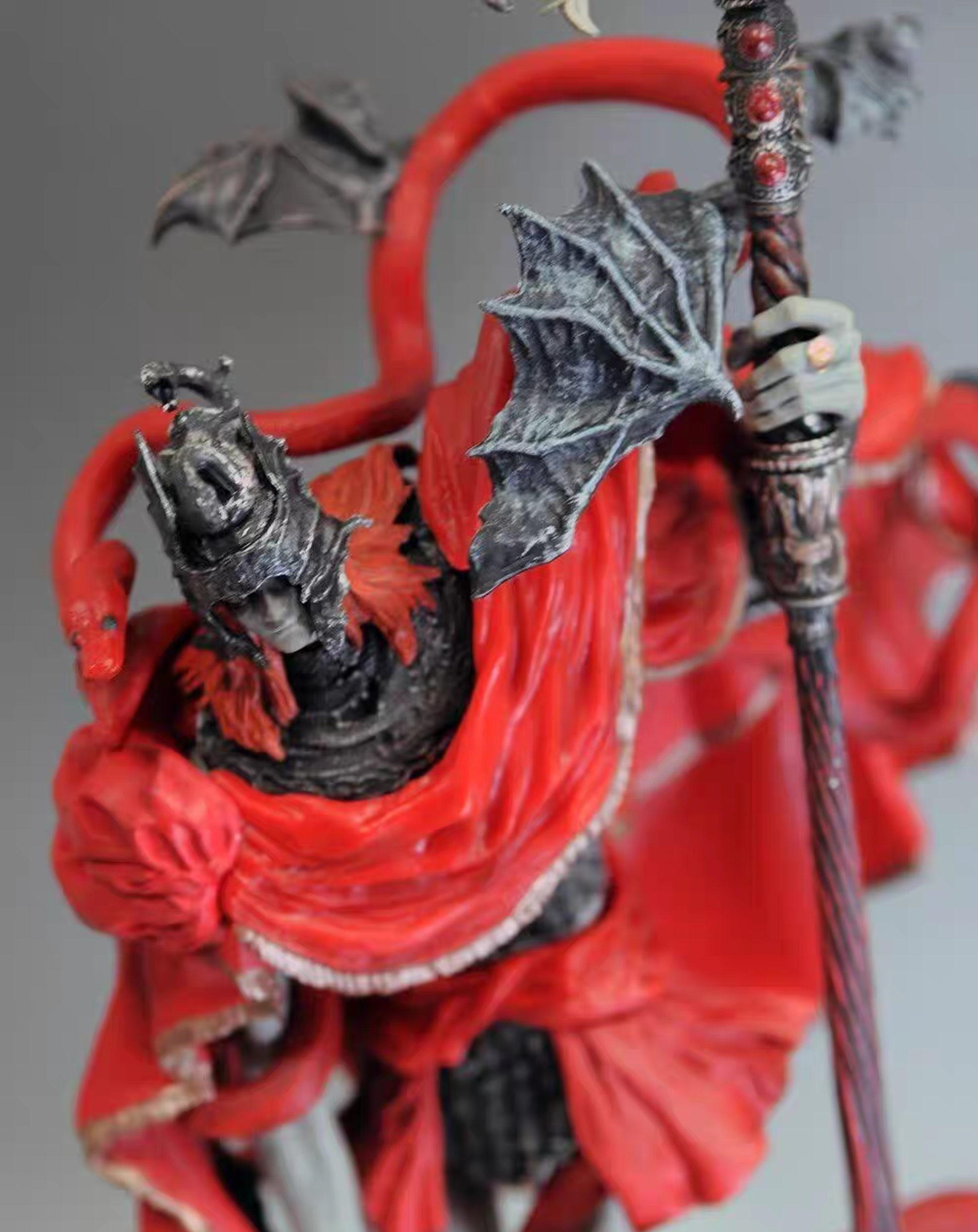 A close-up of a Messmer the Impaler From Elden Ring Video Game figurine or sculpture featuring a dark armored dragon-like creature wrapped in vivid red fabric, with a large bat-like wing and a staff held in a bandaged hand.