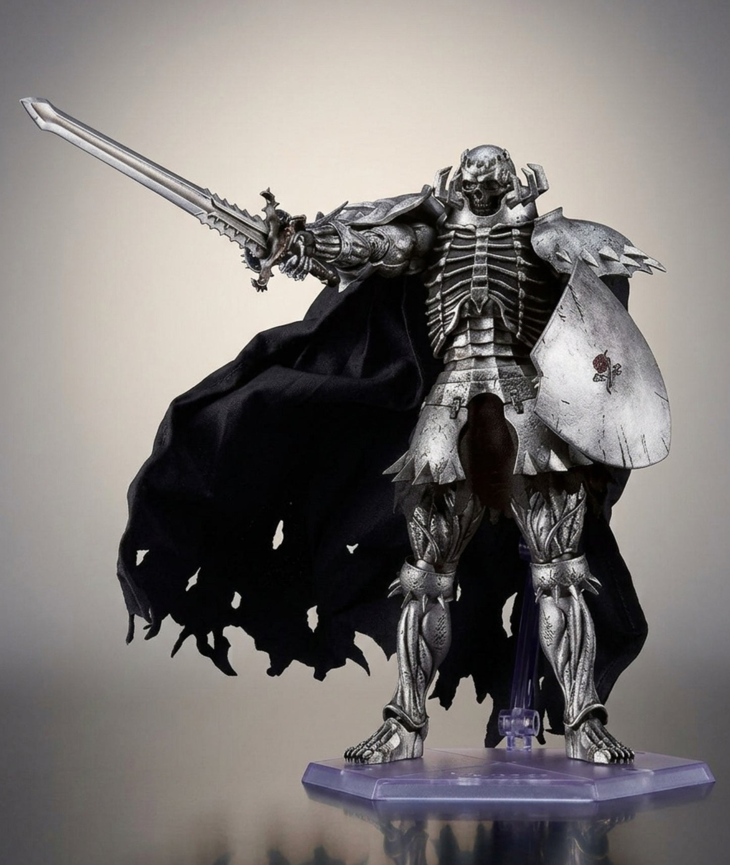 A detailed collectible statue of Skull Knight from Berserk Anime holding a large sword and shield, wearing a flowing black cape, displayed on a clear stand against a neutral studio background.