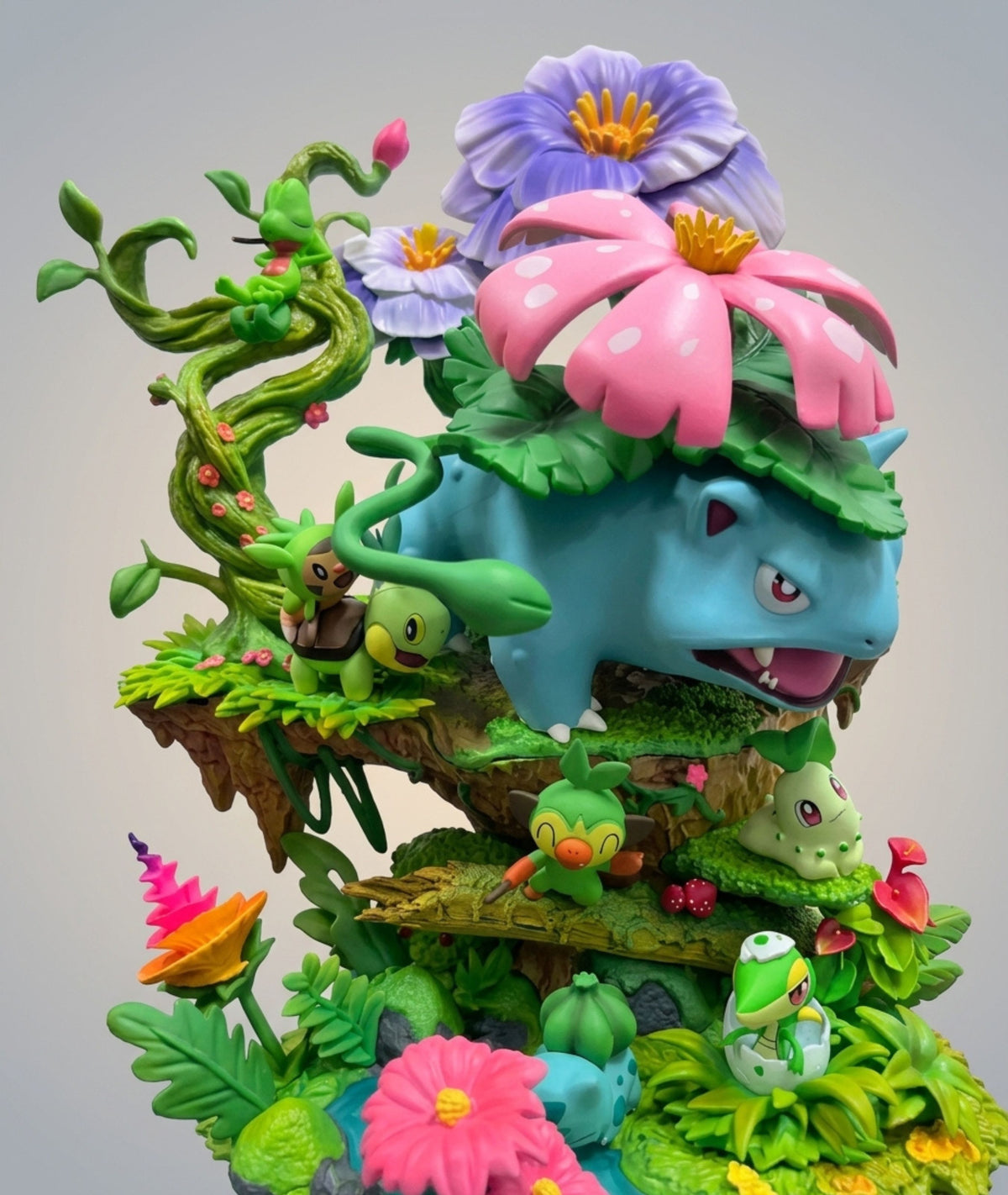 A detailed collectible figurine of Venusaur and his companions from the Pokémon franchise, styled in a lush, fantasy garden scene with colorful flowers, green vines, and foliage against a neutral gray background.