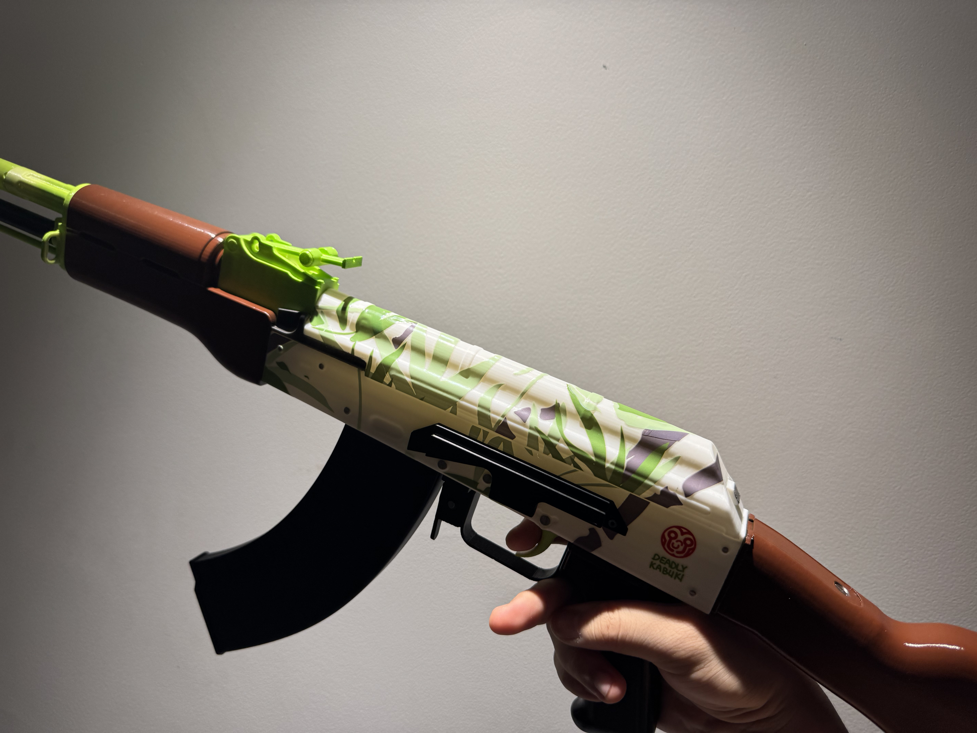 Real life size AK-47 Hydroponic CS2 skin replica — green and teal graffiti pattern detail shot, display stand, studio lighting