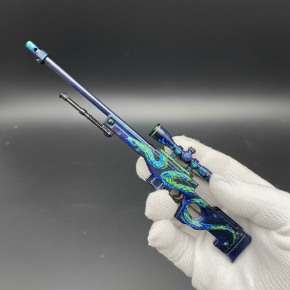 Hand holding Mini AWP Atheris CS2 skin replica — small metal collectible desk piece, black background, front angle view