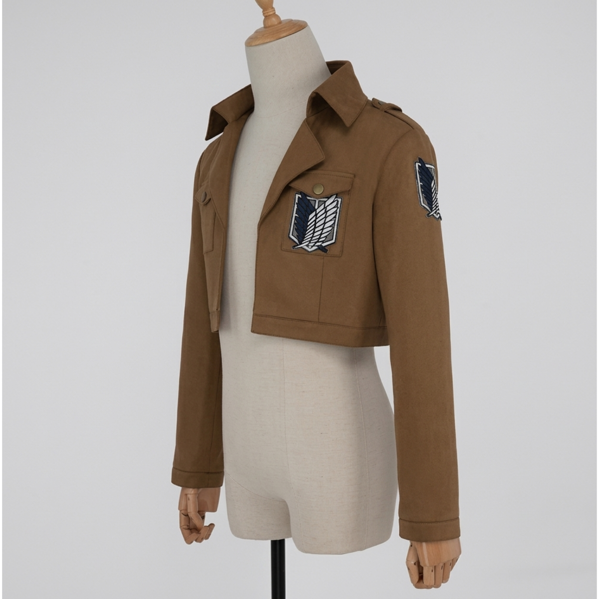 Brown cropped cosplay jacket with collar, flap pockets and wings emblem chest patch, angled front view
