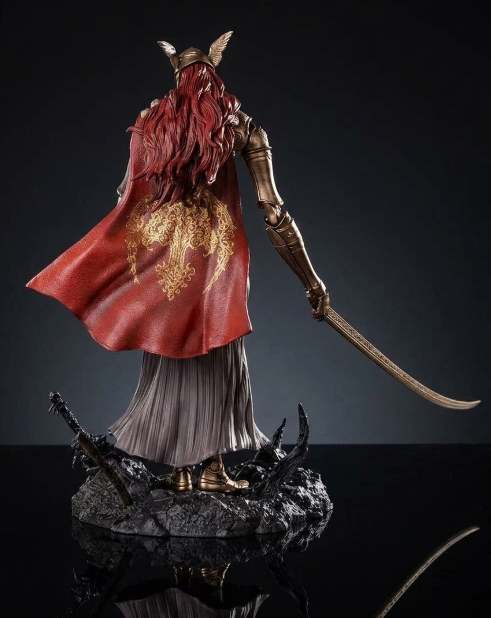 Elden Ring Valkyrie Collectible Figurine shown from the back, featuring long red hair, a flowing red cape with gold patterns, metallic gold armor, and a curved sword, standing on a dark rocky base against a dark studio background.