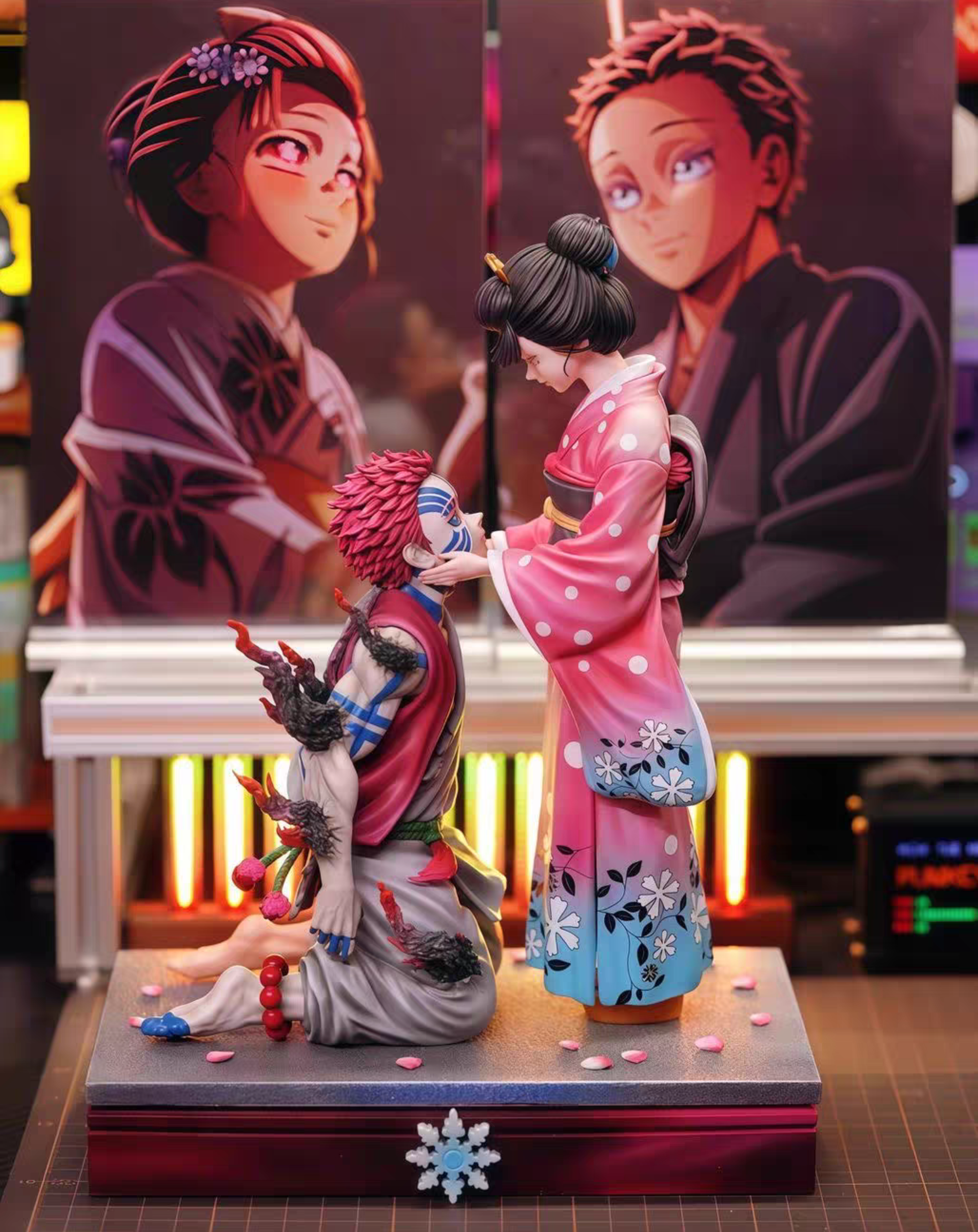 Anime figurine set featuring a kneeling 	Akaza and Koyukiin a red and gray outfit with black hair, and a standing character in a pink and blue kimono, displayed on a base with two large character posters in the background.