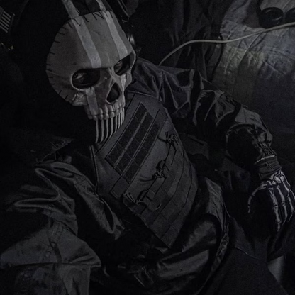 Person wearing full Ghost MW2 operator cosplay — 3D printed skull balaclava mask with tactical plate carrier vest and skeleton gloves, dark moody lighting