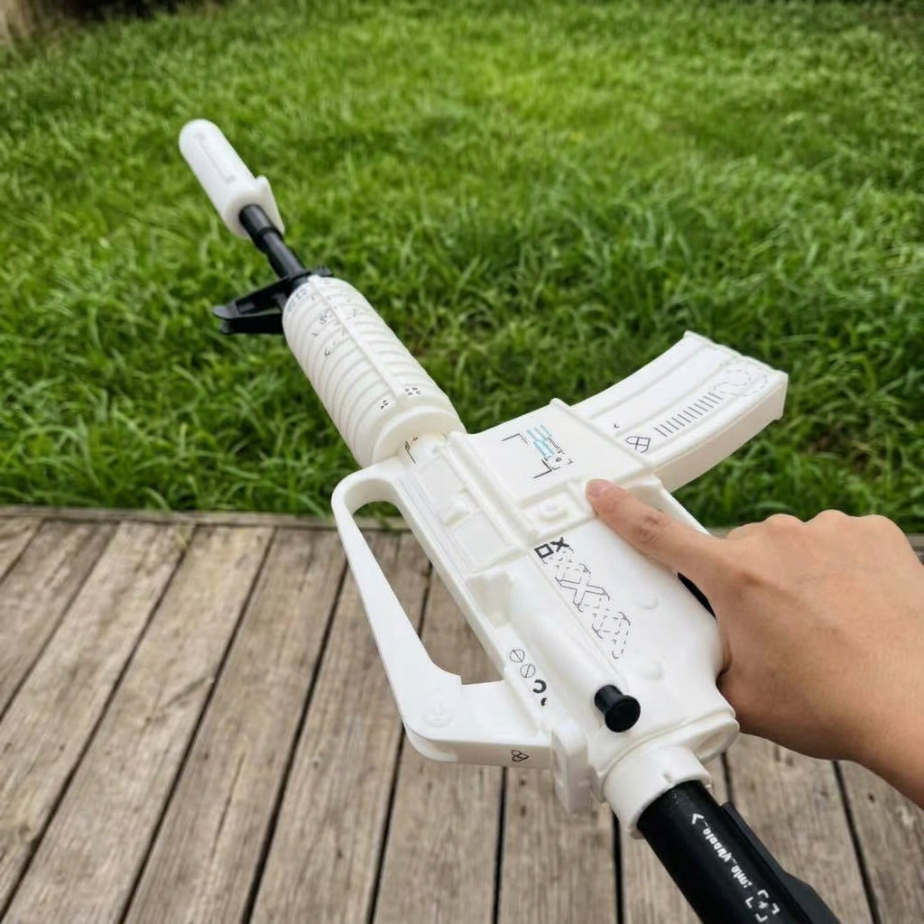 Hand gripping M4A1-S Printstream CS2 life size replica from below — white body with black XX pattern detail, rear underside angle, wooden deck and grass background, natural daylight
