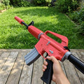 Life size 95cm M4A1-S Rat Rod CS2 replica held in hand outdoors — red and grey skin detail, wooden deck and grass background