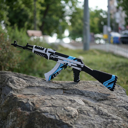 Life size 87cm AK47 Vulcan CS2 replica held in hand outdoors — white and blue geometric skin detail, grass background, front angle view