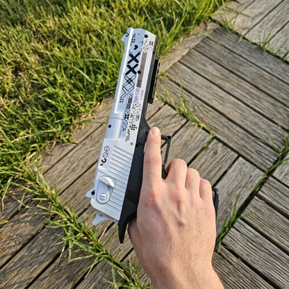 Hand gripping CS2 Desert Eagle Printstream real life replica from above — top down POV view showing white slide with black XX pattern detail, grass and wooden deck outdoor setting