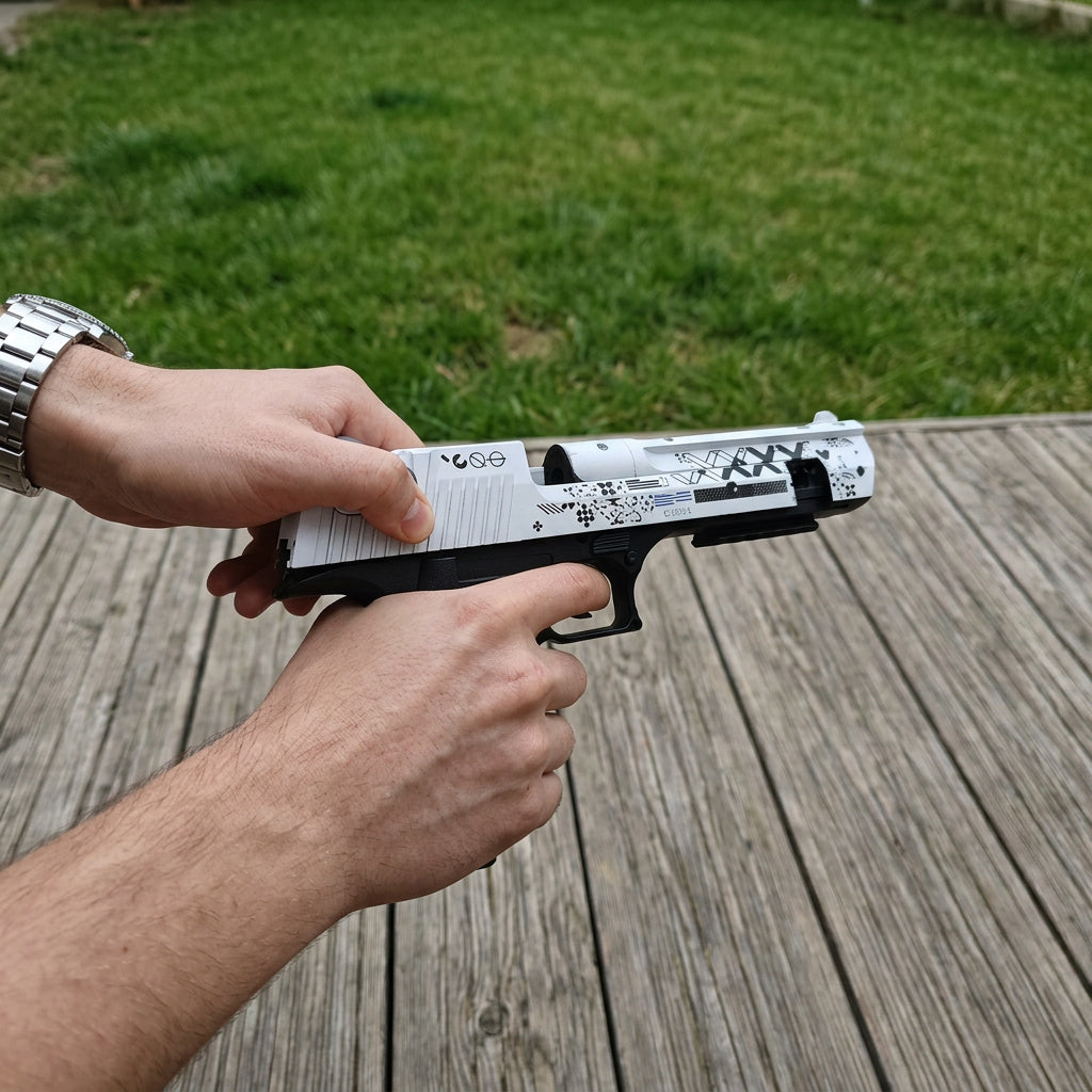 Both hands holding CS2 Desert Eagle Printstream real life replica — slide being pulled back showing moving parts, white and black skin detail, wooden deck outdoor setting