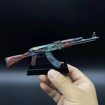 Hand holding CS2 AK47 Fire Serpent mini replica on stand from below, detailed orange and green serpent dragon skin clearly visible