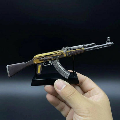 Hand holding CS2 AK47 Fuel Injector mini replica from side angle, displaying intricate gold and silver mechanical skin detail