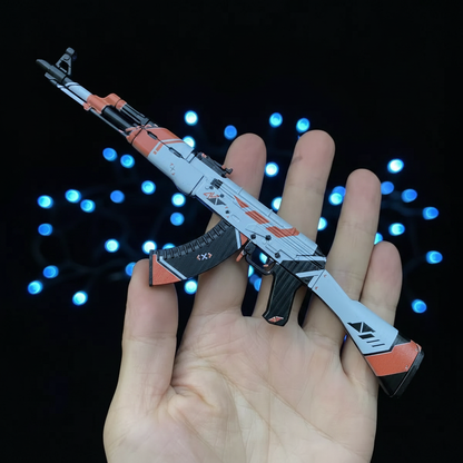 Open palm holding CS2 AK47 Asiimov mini replica, iconic white and orange sci-fi skin with black accents visible from below angle