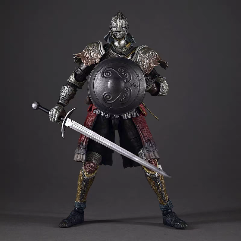 A highly detailed Raging Wolf Elden Ring warrior action figure or collectible statue, dressed in dark metallic armor with red fabric accents and holding a large round shield and a long sword, posed against a dark gray studio background.