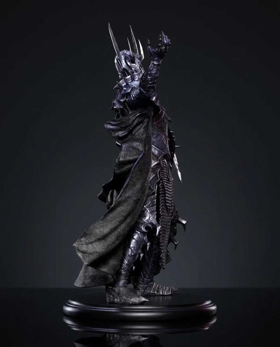 A dark fantasy collectible statue of a Sauron From the Lord Of The Rings, figure with a flowing black cloak, raised clawed hand, and long sword, displayed on a glossy black base against a dark studio background.