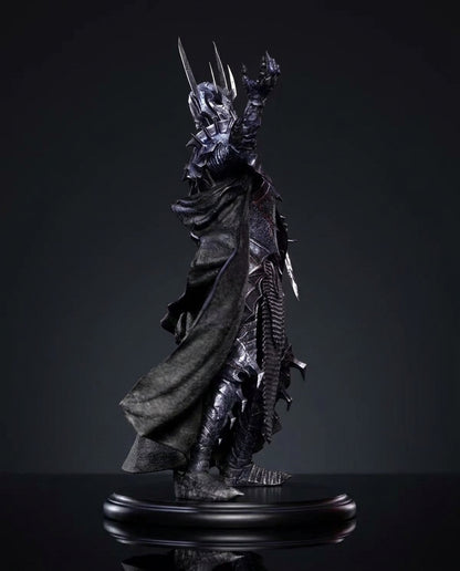 A dark fantasy collectible statue of a Sauron From the Lord Of The Rings, figure with a flowing black cloak, raised clawed hand, and long sword, displayed on a glossy black base against a dark studio background.