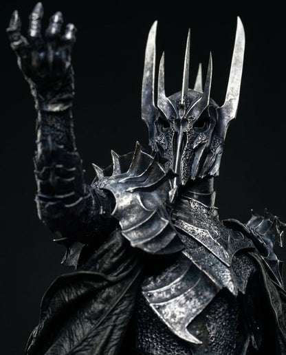 A close-up of a Lord Of the Rings character named Sauron, armored character figure with a black textured body, spiked silver helmet, raised clawed hand, and dark cape against a black background.