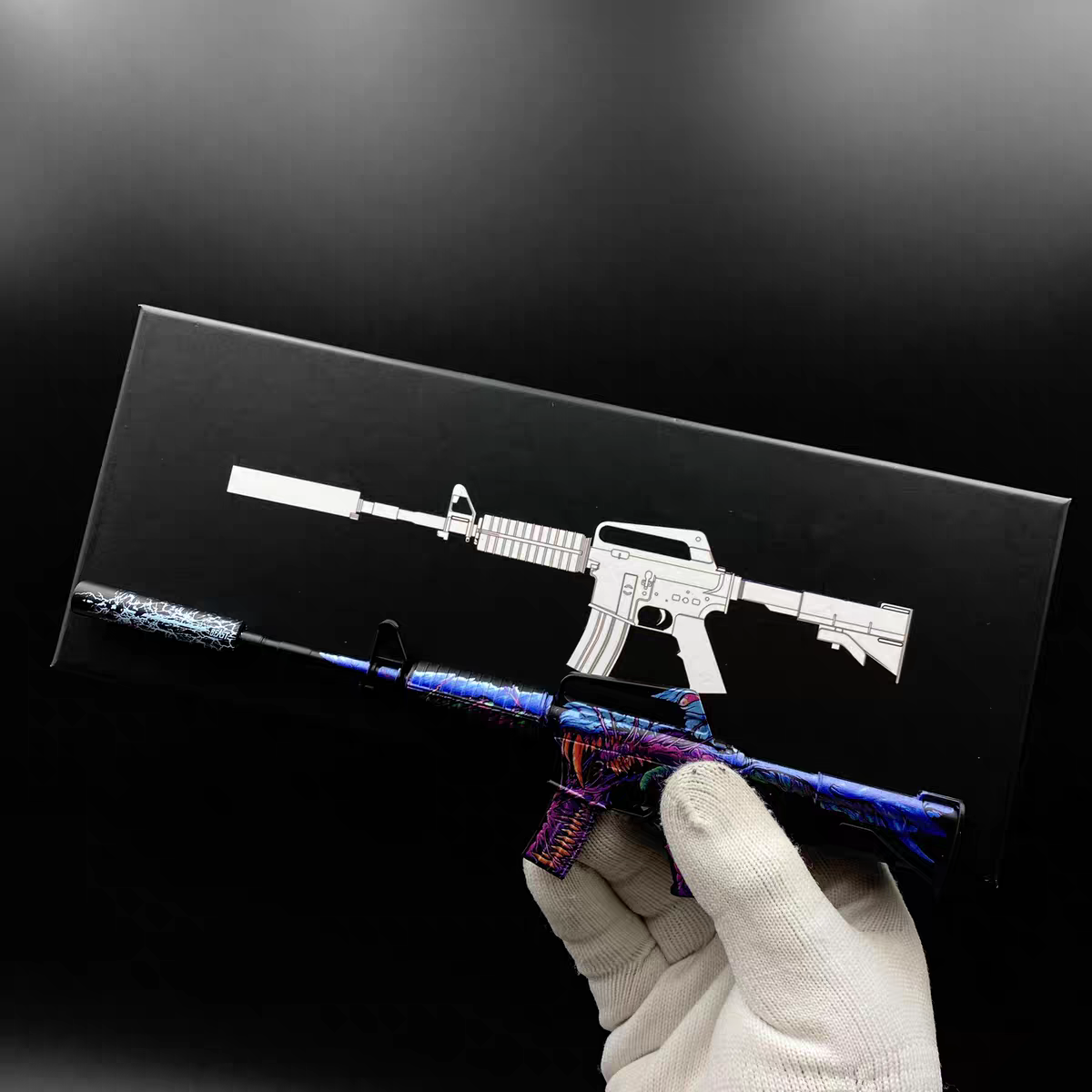 Hand holding Mini M4A1-S Hyper Beast CS2 skin replica — small metal collectible desk piece, black background, front angle view