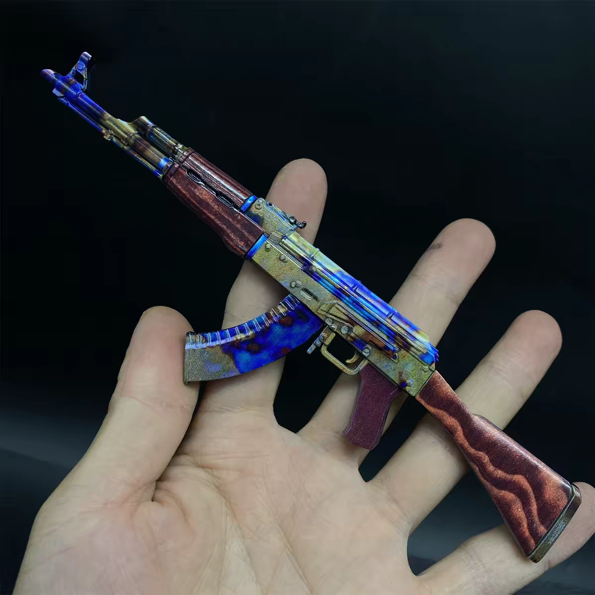 Hand holding CS2 AK47 Case Hardened mini replica showing unique blue gold splash pattern across barrel and wood stock close-up