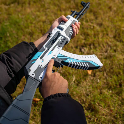 Both hands holding AK47 Vulcan CS2 life size replica from above — white and blue geometric skin detail, removable magazine visible, grass background, overhead angle showing full body of weapon