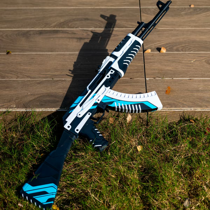 AK47 Vulcan CS2 life size replica standing upright leaning against wooden deck — white and blue geometric skin with dramatic shadow, grass and autumn leaves ground, full length front view