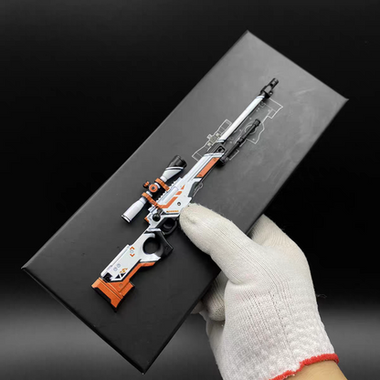 Hand holding Mini AWP Asiimov CS2 skin replica — small metal collectible desk piece, black background, front angle view