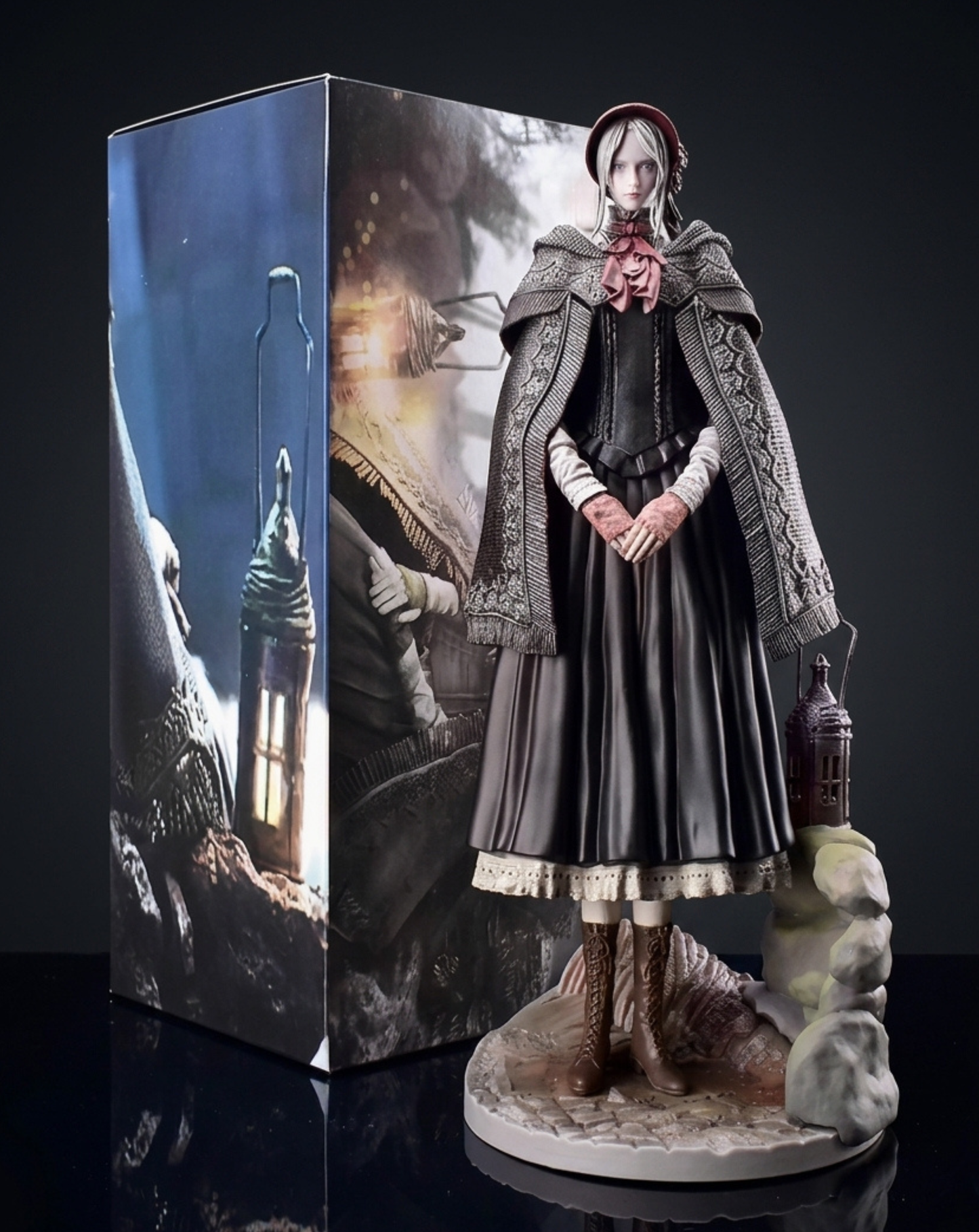 A detailed collectible Doll figurine of from Bloodborne, standing on a stone base next to a matching illustrated display box, set against a dark studio background.