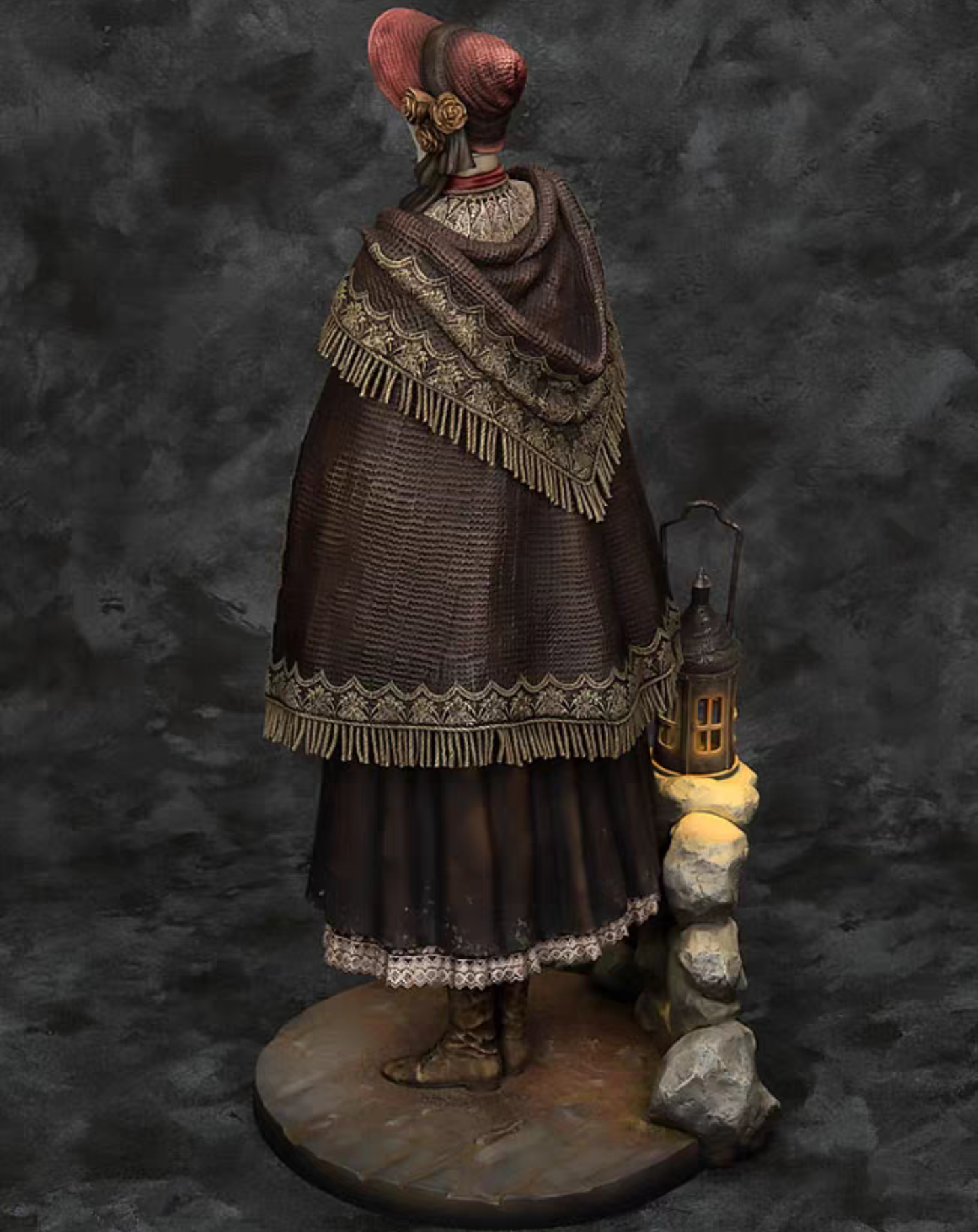 A detailed The Doll Bloodborne figurine of a woman from behind, wearing a dark brown fringed cloak, a red headpiece, and boots, standing on a round base next to a lantern and small rocks against a dark textured backdrop.
