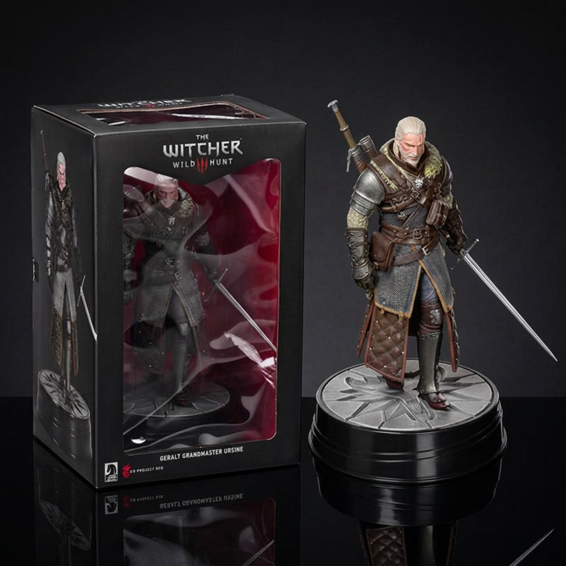 A collectible action figure of Geralt of Rivia from The Witcher Wild Hunt standing beside its retail box on a dark reflective surface. The figure is dressed in dark gray and brown armor with a sword on each shoulder, posed next to a black display box featuring the Witcher branding.